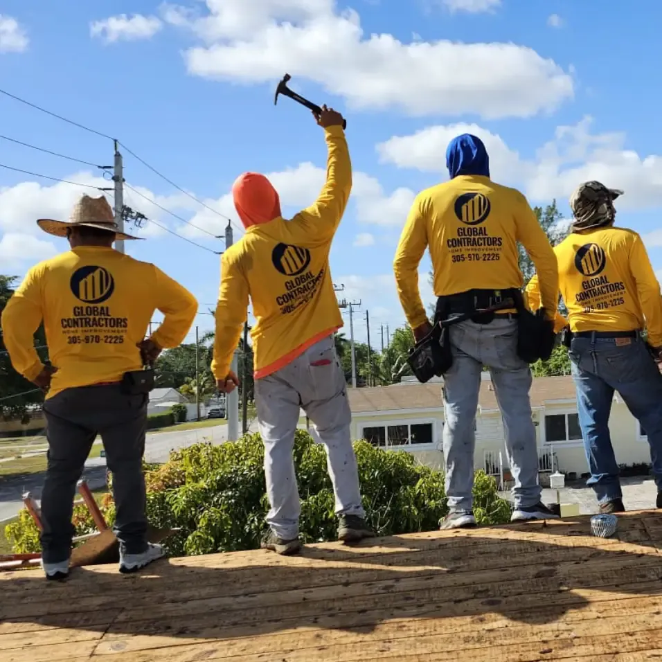 Cuadrilla de Global Contractors en un techo, uno levantando un martillo