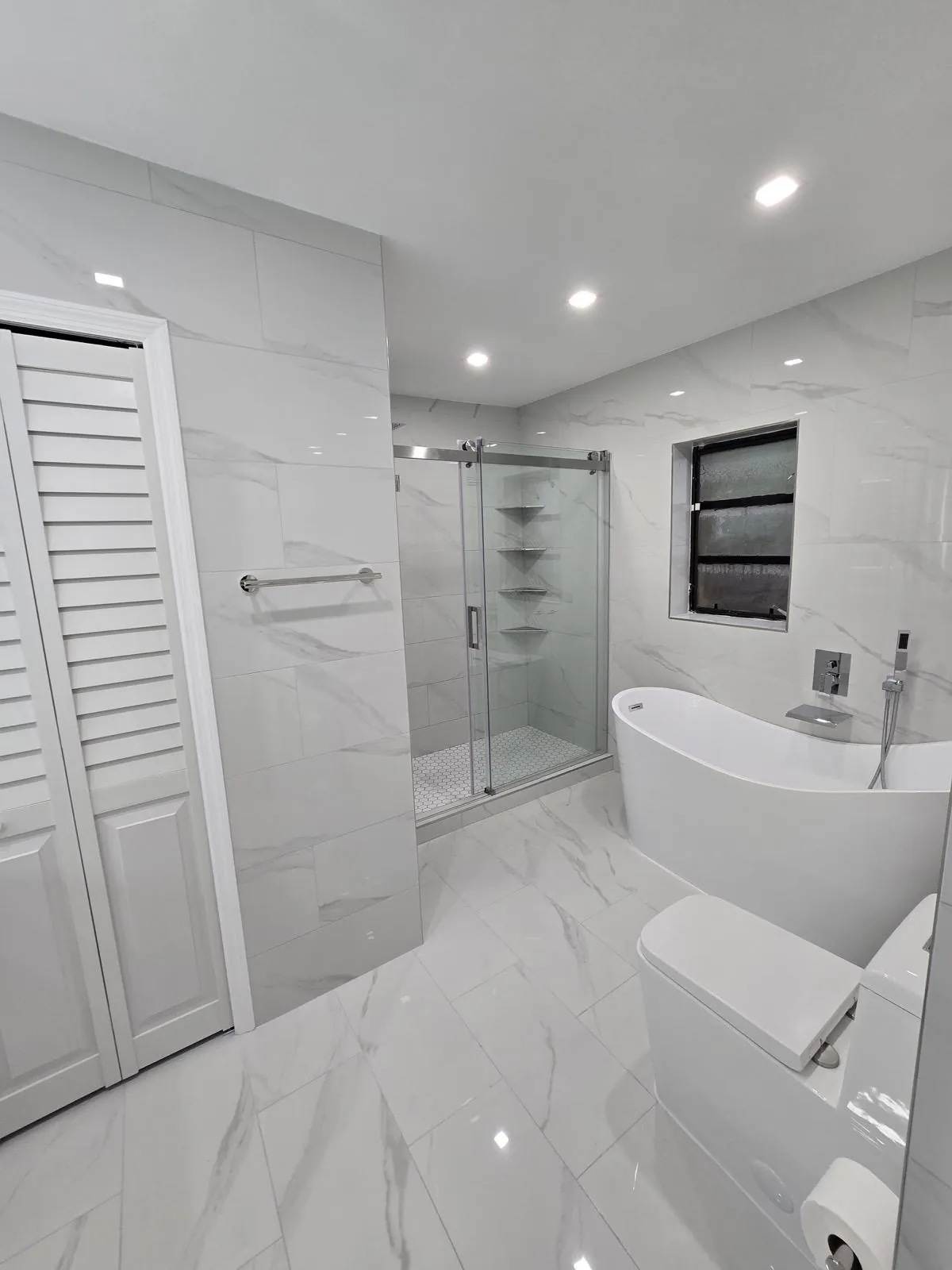 Finished bathroom with a freestanding tub and glass shower in marble-look tile