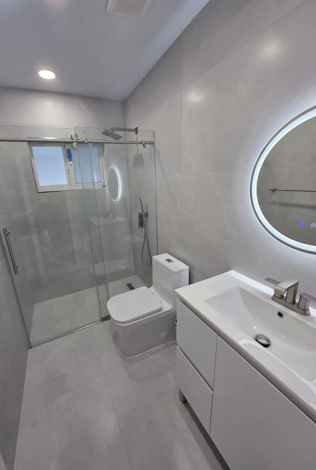 Finished bathroom with a glass shower and a round LED mirror