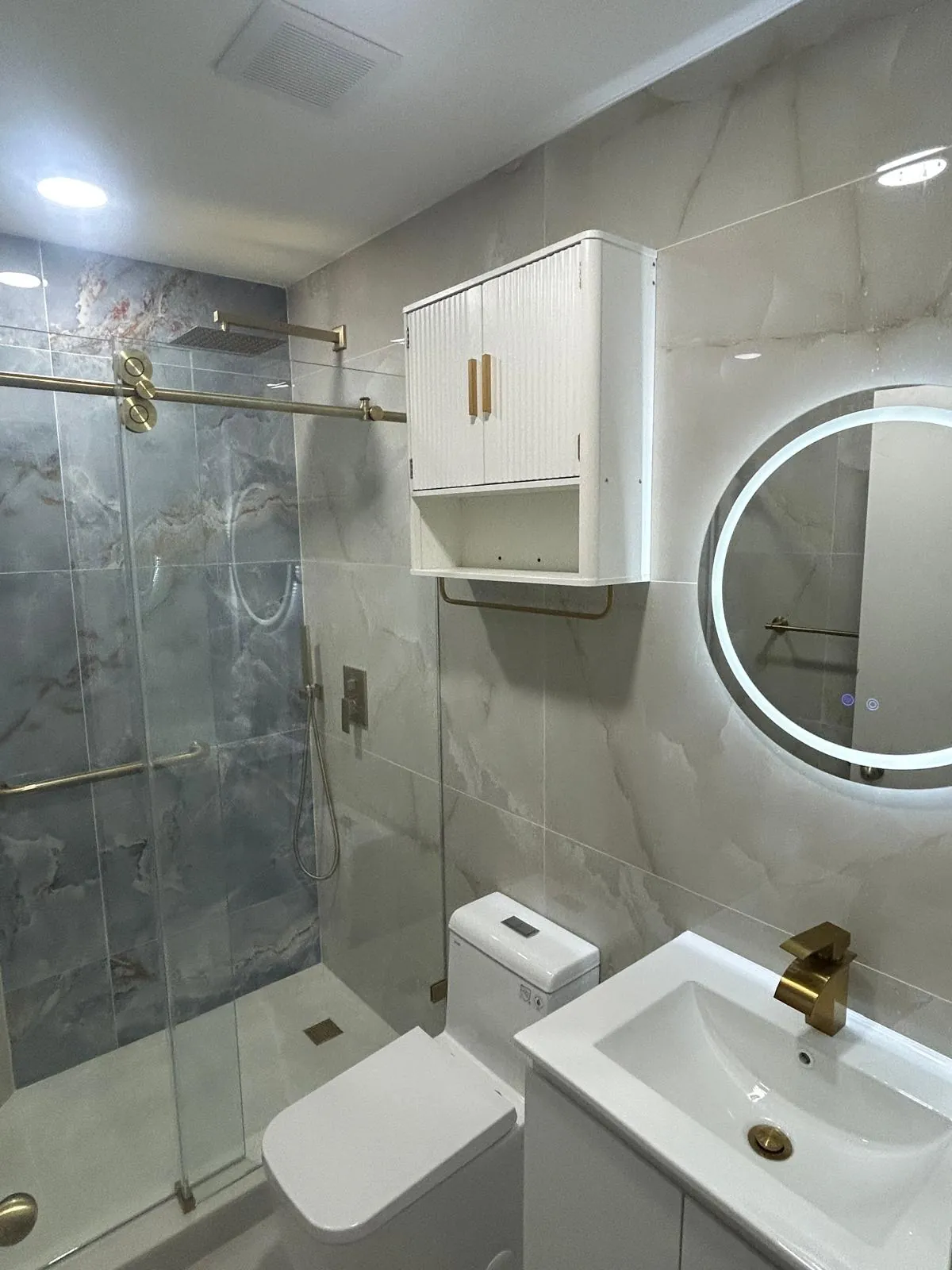 Finished bathroom with gold fixtures and a round LED mirror