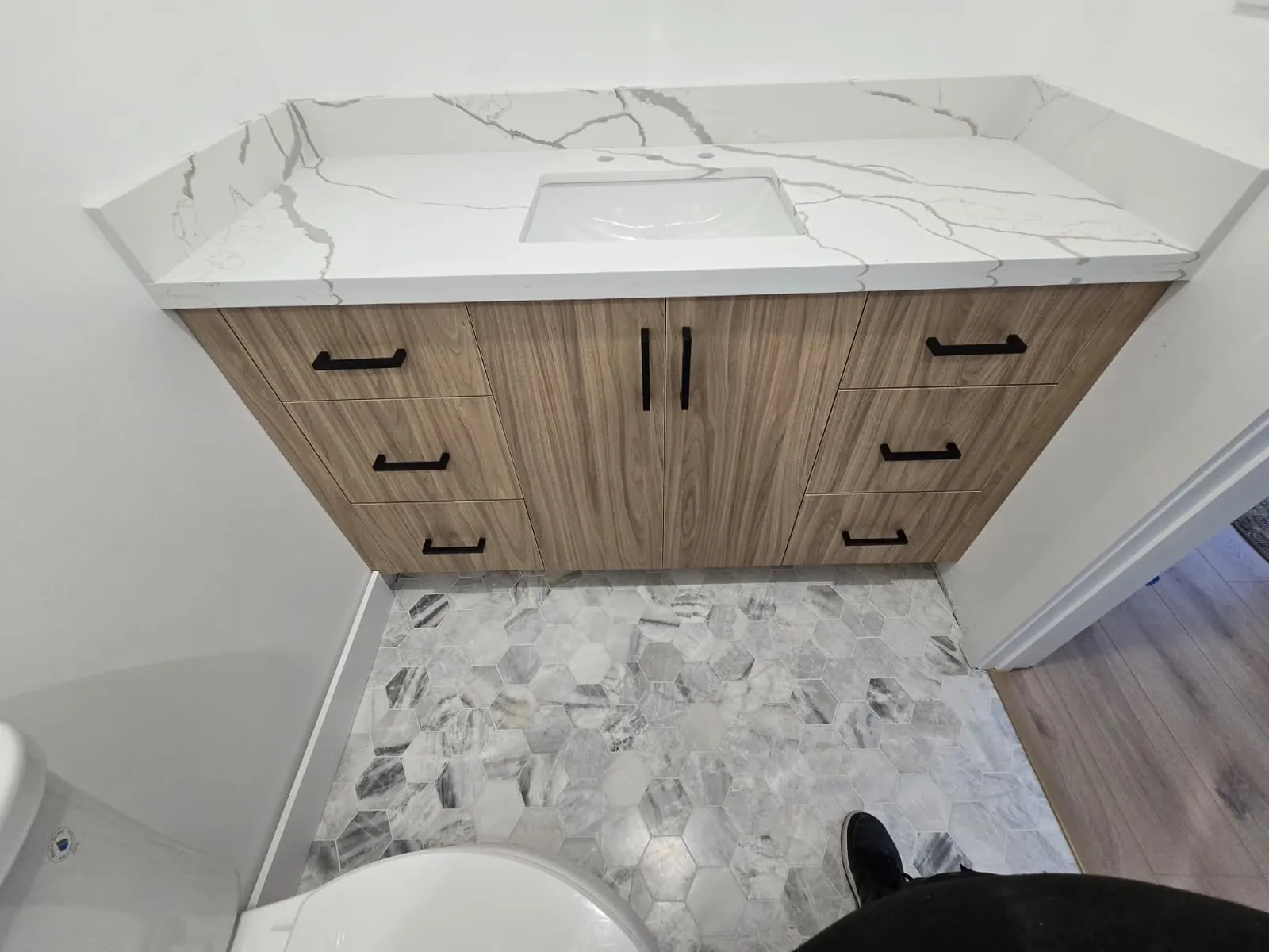 Finished wood vanity with a marble-look top and hexagon floor tile