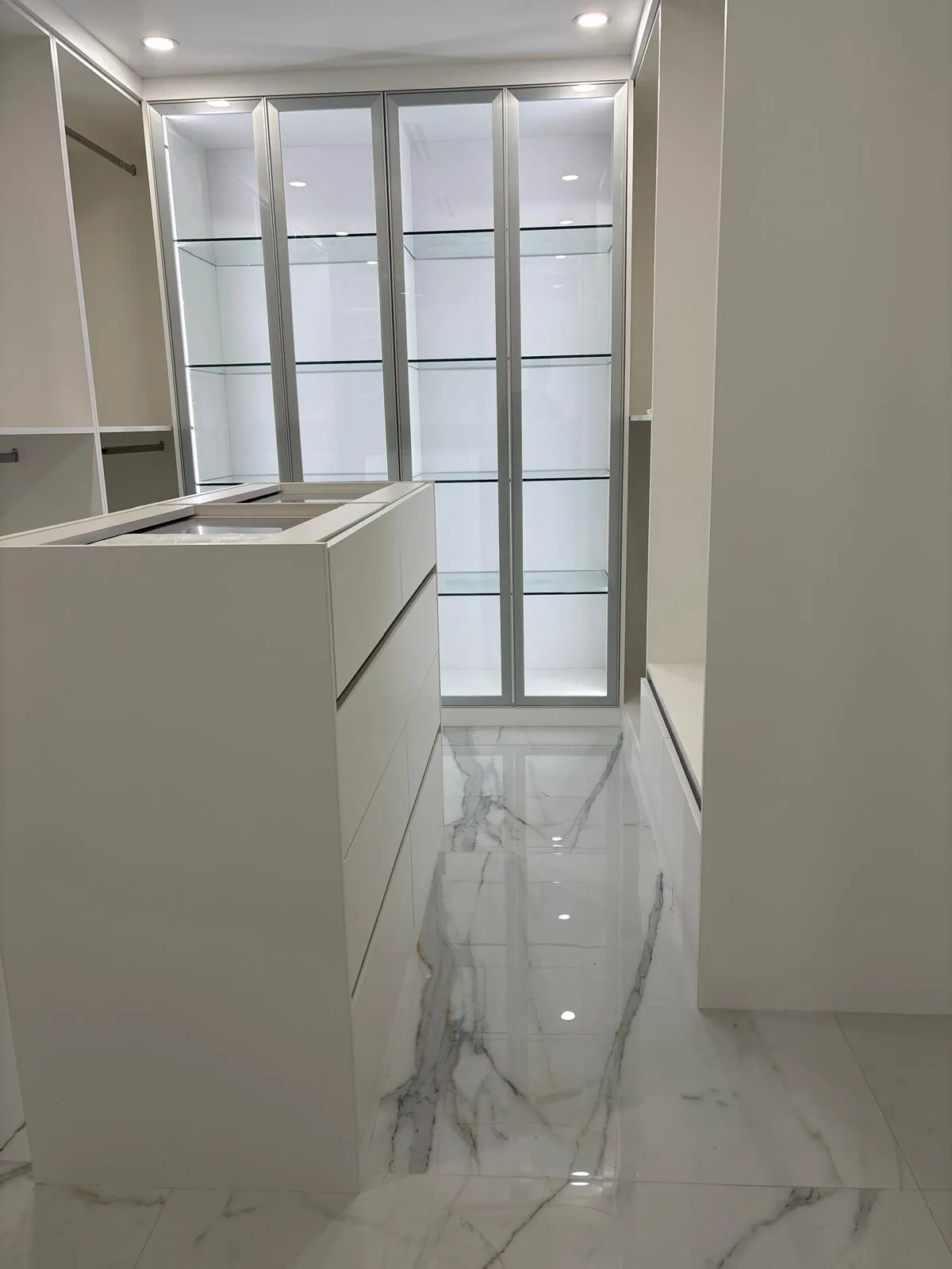 Walk-in closet with lit glass cabinets and an island
