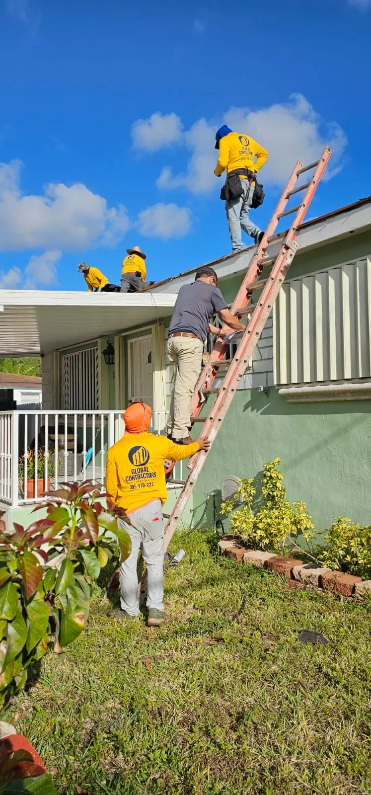 Cuadrilla de Global Contractors trabajando desde una escalera en el borde del techo