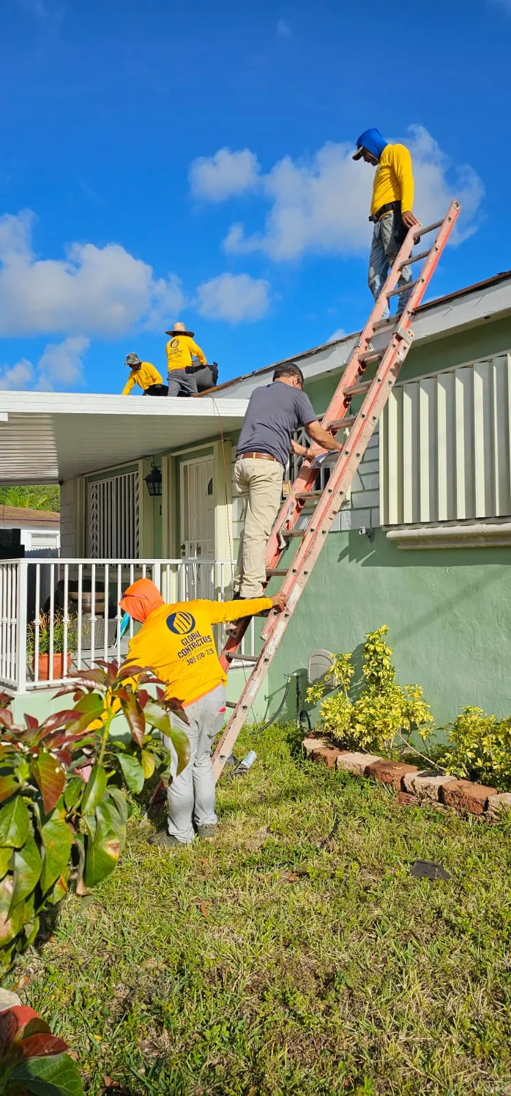 Cuadrilla de Global Contractors trabajando desde una escalera en el borde del techo