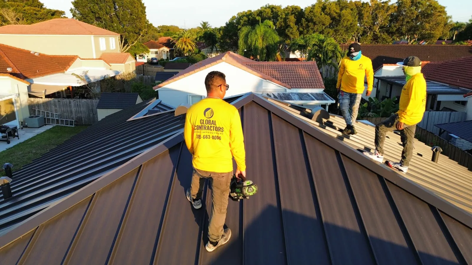 Cuadrilla de Global Contractors con camisas amarillas en un techo de metal de junta alzada oscuro nuevo, vista aérea
