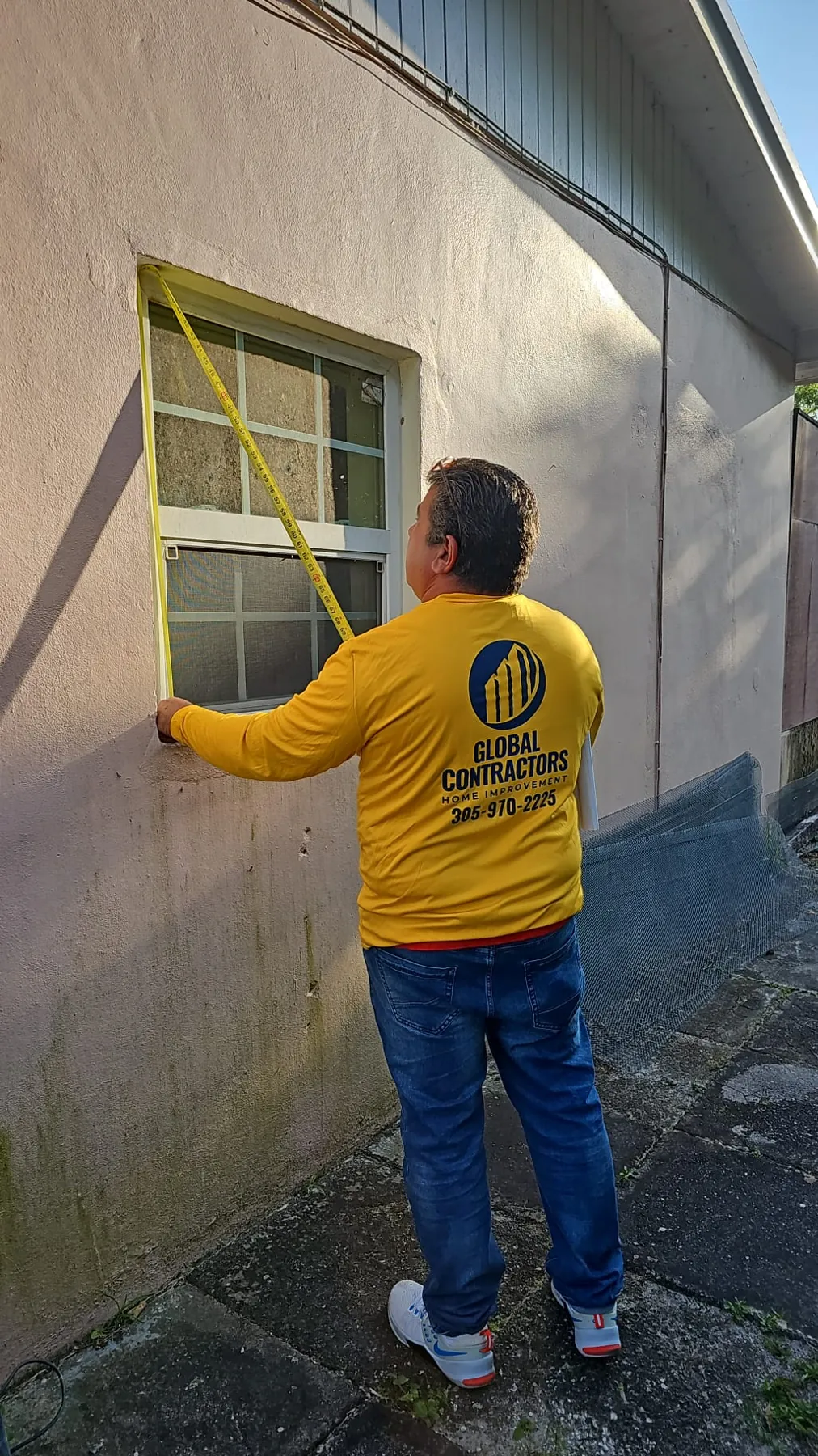 Instalador de Global Contractors midiendo una ventana desde afuera