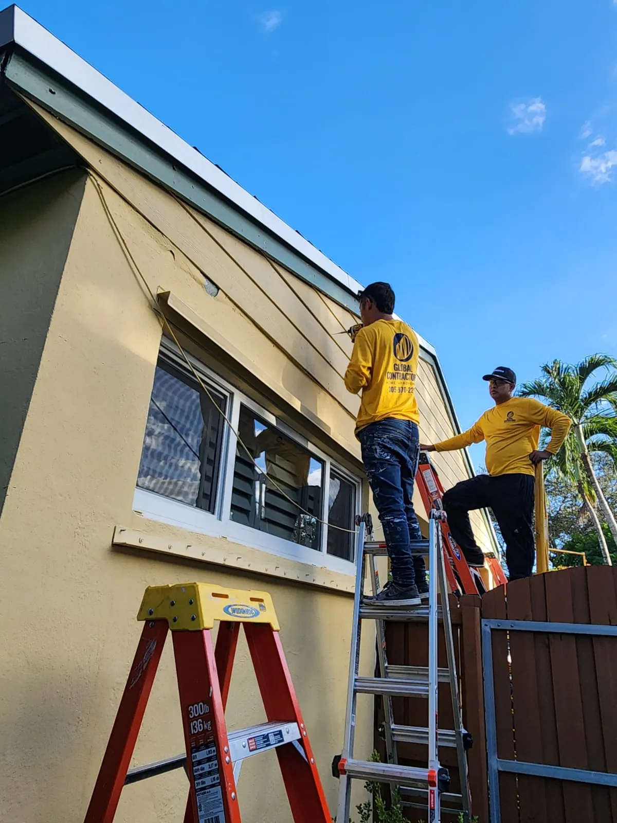 Cuadrilla de Global Contractors instalando ventanas de impacto desde una escalera